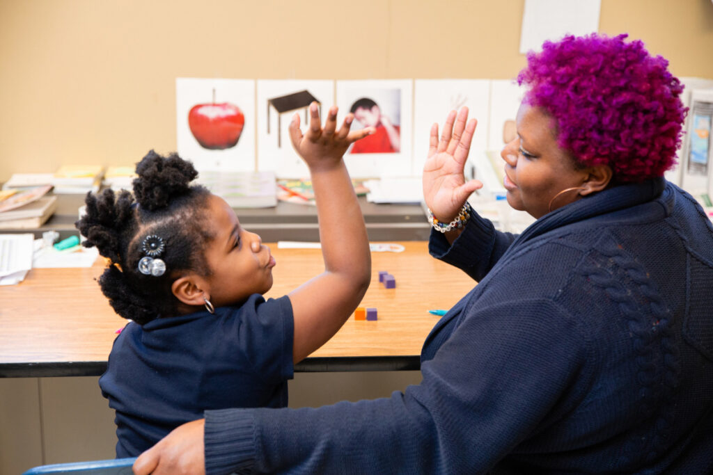 Teacher with purple hair giving high-five to young student during literacy tutoring session