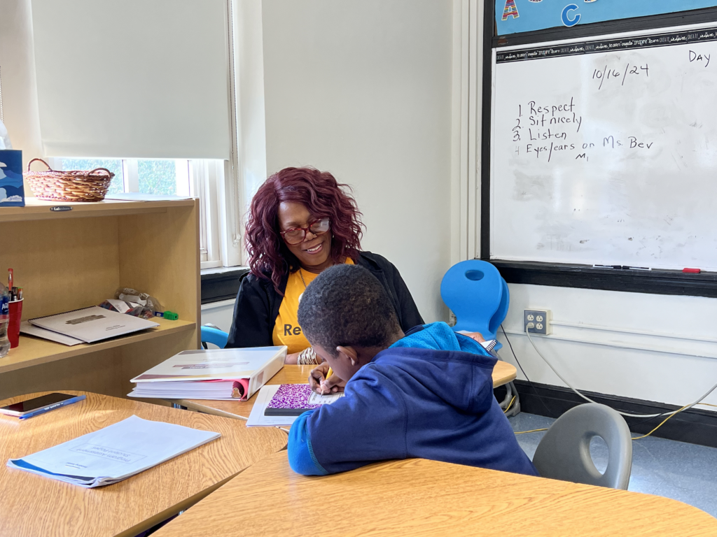 Literacy specialist tutoring elementary student at desk in classroom